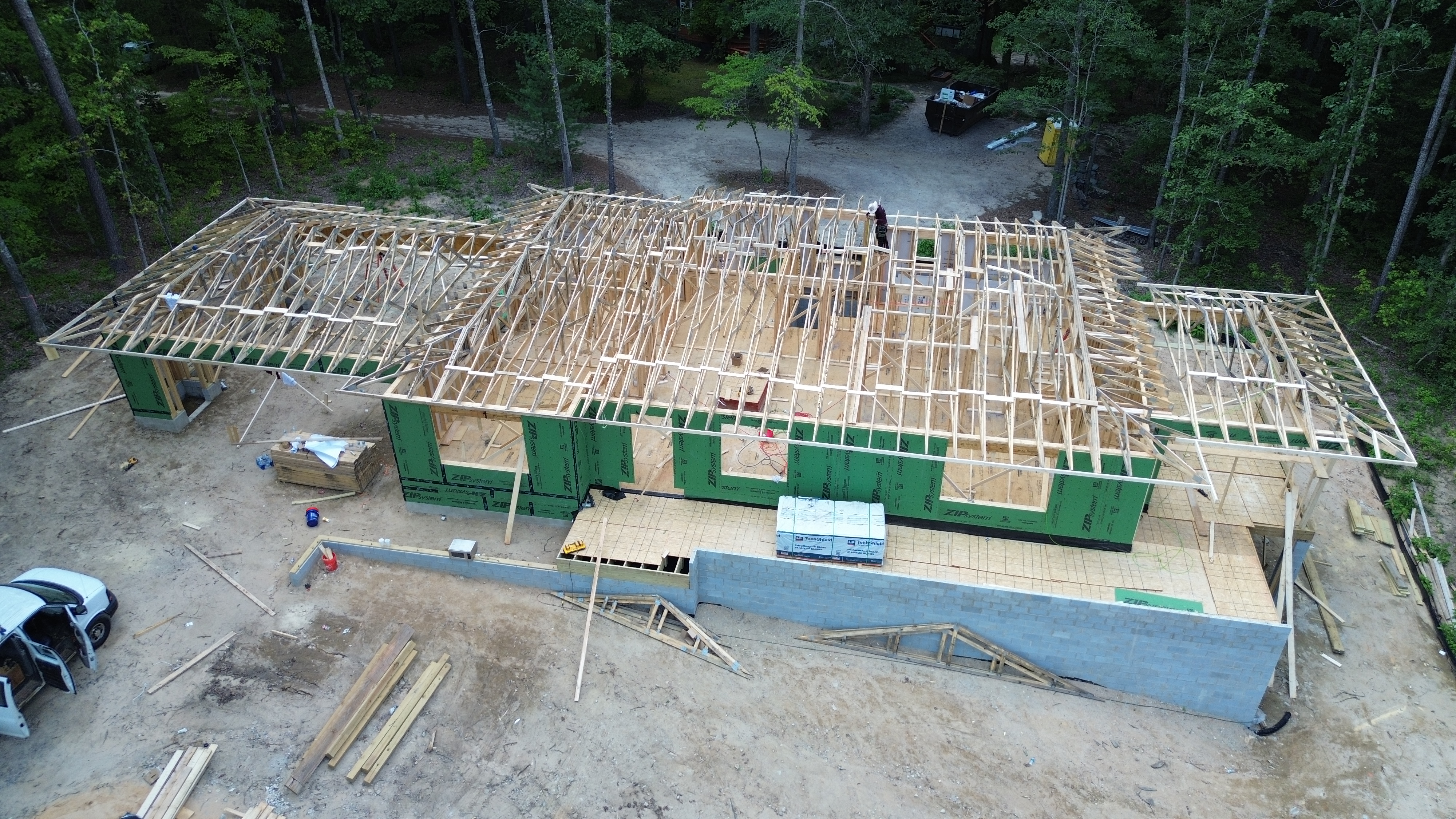 An aerial photo of a large house under construction with trusses installed, but no roof sheathing. 