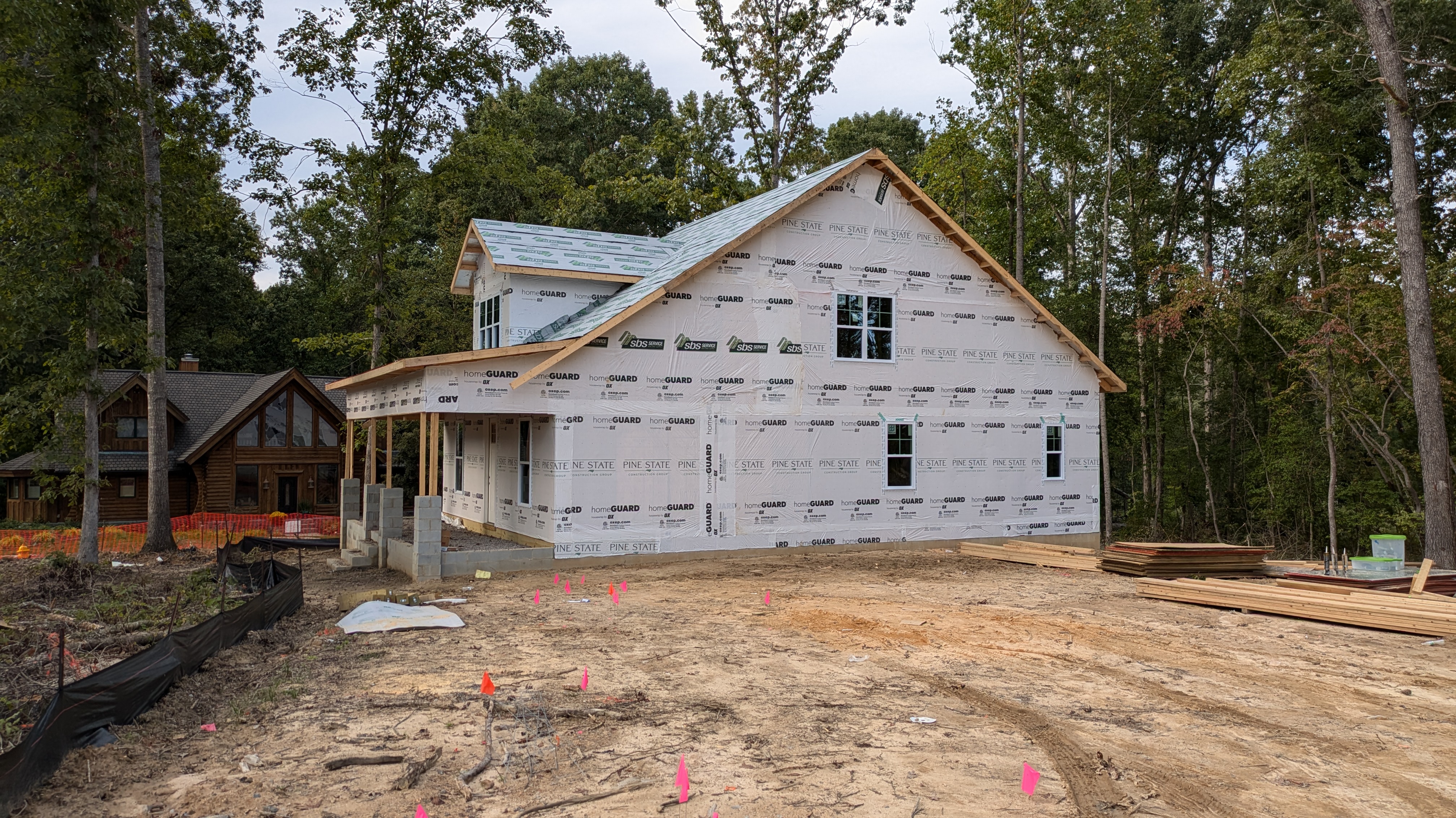 Framed 1.5 story house with house wrap applied, but no siding or shingles on the roof. Dirt lot in the foreground. 