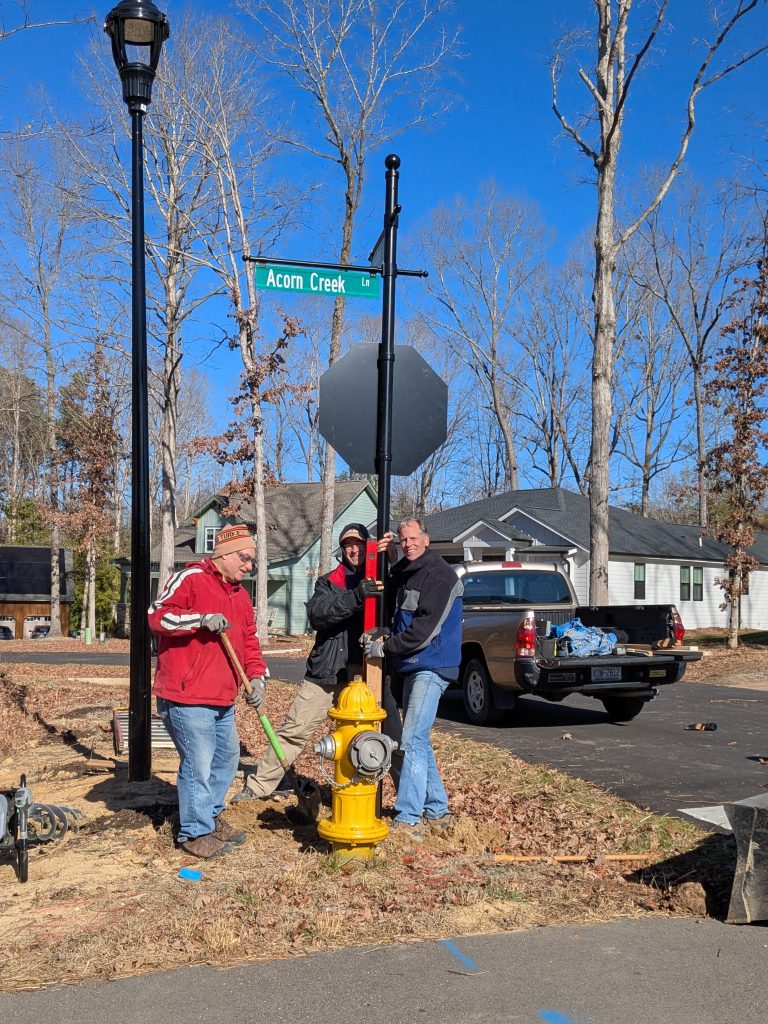 Three men with shovels and a level gathered around a pole with a stop sign and street signs being installed.