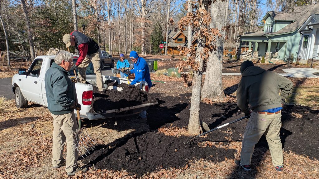 People unloading mulch from the back of a pickup and spreading it with rakes.